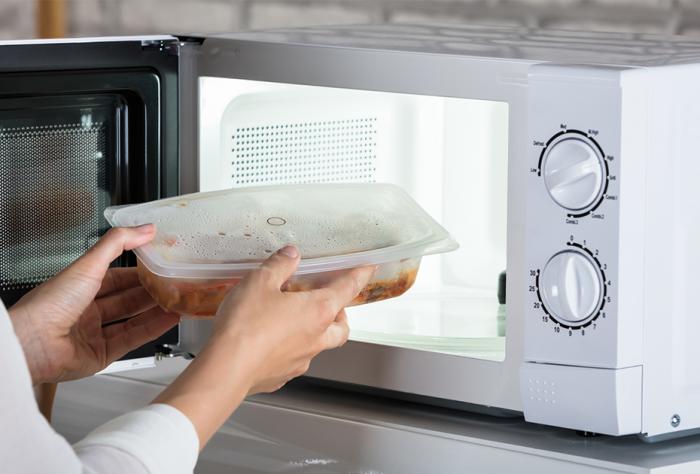 Person removing meal from microwave wrapped in plastic box